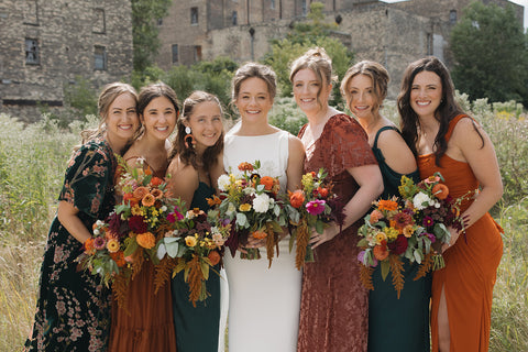 DIY bridal flowers from First Roots Farm Bride with bridesmaids holding floral bouquets in a field.
