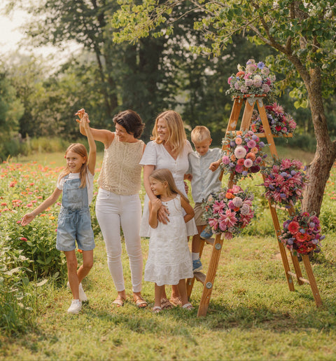 Family with children standing in a field with floral decorations on wooden ladders at First Roots Farm photo captured by Katiebee Photography
