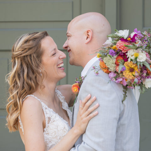 Bride and groom embracing with a colorful bouquet of flowers.