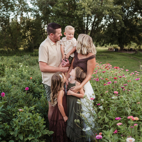 Family of five standing in a field with flowers and trees in the background at First Roots Farm
