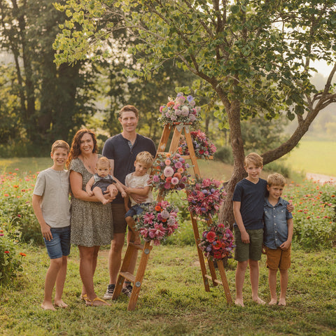 Family of seven standing in a field with floral decorations on a ladder.