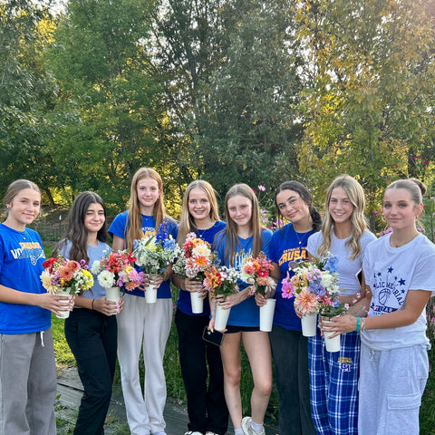 Group of young women holding flowers outdoors with trees in the background