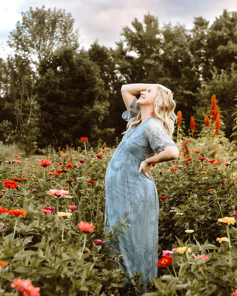 Woman in a blue dress standing in a field of flowers with trees in the background