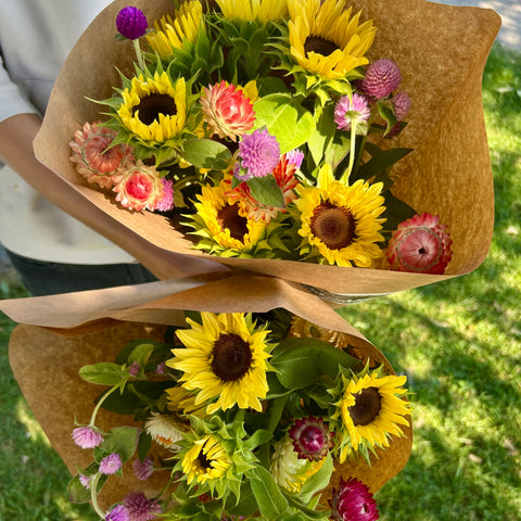 Bouquet of sunflowers and pink flowers wrapped in brown paper on a grassy background