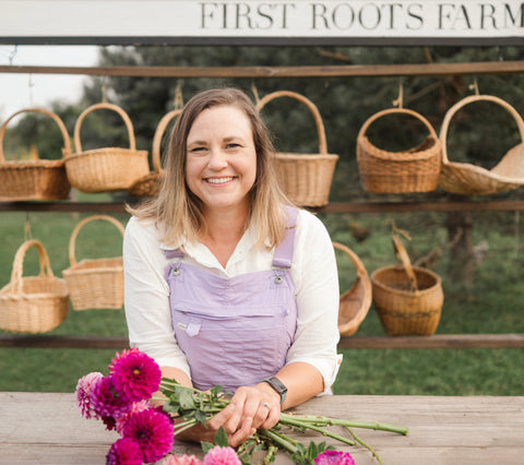 Janell Vera holding flowers in front of a display of wicker baskets at First Roots Farm.
