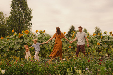 Family of four walking hand-in-hand through a sunflower field on a cloudy day.