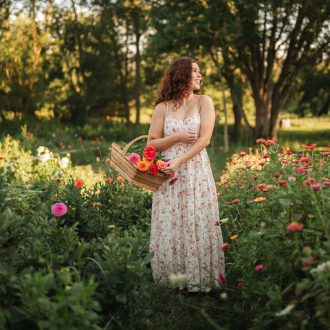 Woman in a floral dress holding a basket of flowers in a garden.