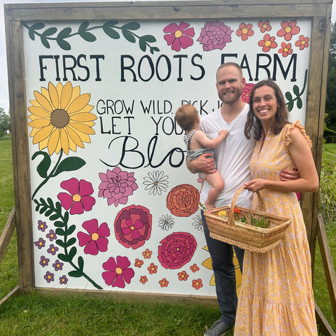 Family posing in front of 'First Roots Farm' sign with floral designs